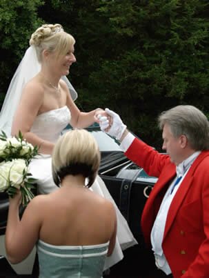 Wedding toastmaster helping bride from carriage as she arrives for her wedding reception