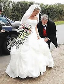 English toastmaster Richard Palmer assisting a bride with her wedding dress as she arrives at the church